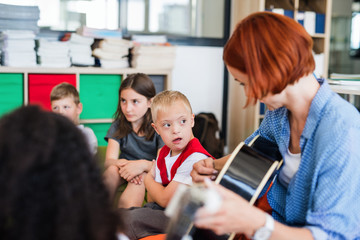 A down-syndrome boy with school kids and teacher sitting in class, playing guitar.
