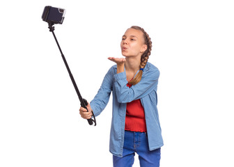 Happy teen girl making selfie with stick and sending an air kiss. Teenager posing to smartphone on selfie stick, isolated on white background. Child taking selfie on mobile phone for social network.