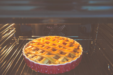 Fresh baked golden apple pie in red dish in oven at kitchen