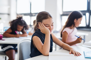 A small tired school girl sitting at the desk in classroom, sleeping.