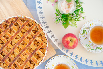 Fresh baked apple pie, cup of tea and flowers on a table