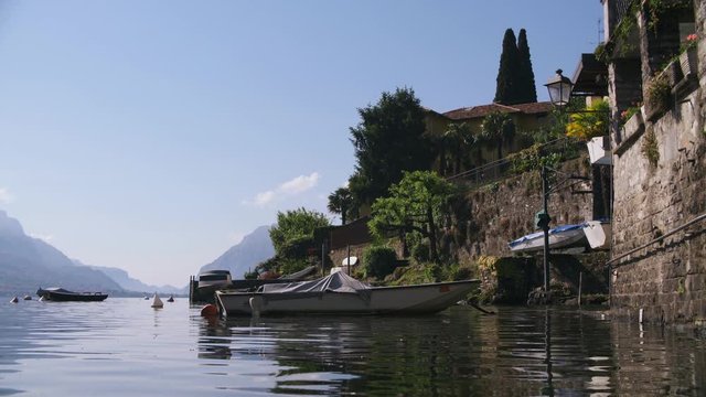 View of small boat moored at pier by old beautiful villa on Como lake in Italy. Medieval village by beautiful mountain lake on sunny day