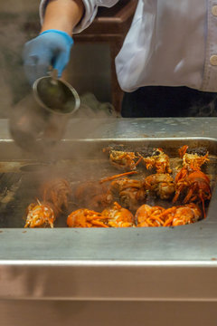 Vertical photo of chef grilling delicious crayfish on smoky stove