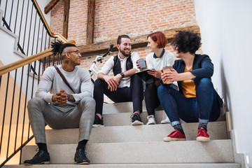 Group of young businesspeople sitting on stairs indoors, talking.