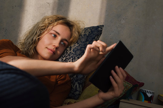 Portrait of young woman lying on bed using E-book reader