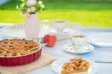 Fresh baked apple pie, cup of tea and flowers on a table