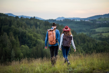 Rear view of young tourist couple travellers with backpacks hiking in nature.