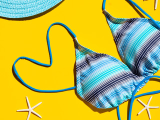 Travel concept on yellow background. Straw hat and blue bikini. Minimal summer flat lay with hard light and shadows. Heart shape