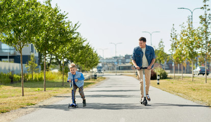 family, leisure and fatherhood concept - happy father spending time with little son riding scooters...