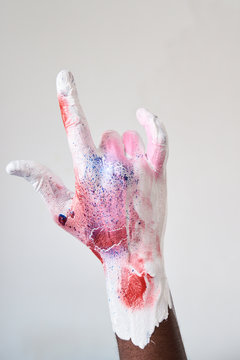 Artist hand covered in colorful paint while doing sign of the horns