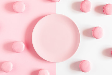 Pink macaroons, empty pink plate on pink and white background. Sweet background. Flat lay, top view, copy space