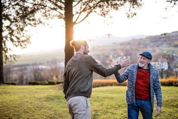 Senior father and his son on walk in nature, giving high five.