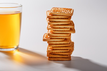A stack of golden wheat cookies and a mug of fragrant green tea in on a gray background. Cookies laid out in a breakfast column and a golden highlight with tea mugs