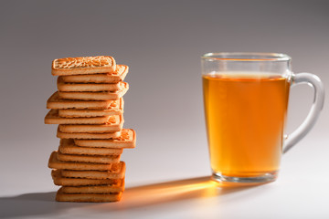 A stack of golden wheat cookies and a mug of fragrant green tea in on a gray background. Cookies laid out in a breakfast column and a golden highlight with tea mugs