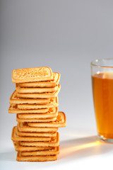 Fototapeta na wymiar A stack of golden wheat cookies and a mug of fragrant green tea in on a gray background. Cookies laid out in a breakfast column and a golden highlight with tea mugs