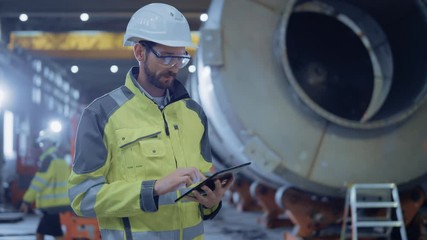 Heavy Industry Engineer Walk Through Pipe Manufacturing Factory, Use Digital Tablet Computer. Facility for Construction of Oil, Gas and Fuel Pipeline Transportation Products. Side View Slow Motion - Powered by Adobe