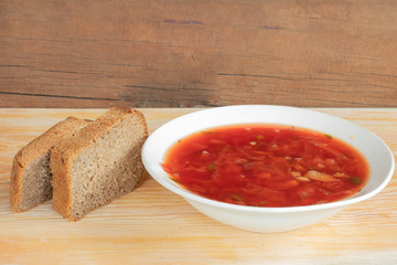 borsch in a white plate on a wooden background and bread
