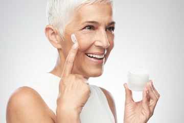 Gorgeous smiling Caucasian senior woman trying out new anti age cream. Beauty photography.