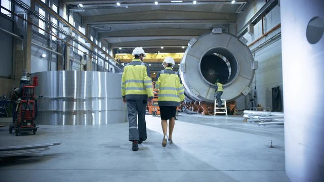 Two Heavy Industry Engineers Walk Through Pipe Manufacturing Factory. Facility for Construction of Oil, Gas and Fuel Pipeline Transportation Products. Following Back View Camera Shot