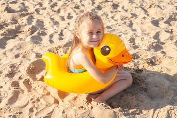 Little girl with inflatable circle in the shape of a duck on the beach