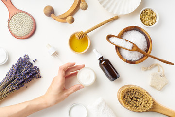Spa beauty skincare flatlay with lavender and fresh ingredients or homemade beauty products and scrubs. Female hand holding a jar of cream. Overhead view, copy space.