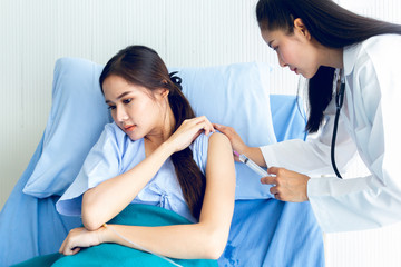 Obraz premium Asian young female doctor being injecting a young woman patient, who shows anxious facial expression and lying in bed In the room to treat the illness better.