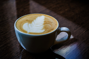 A white cup of cappuccino with latte art on a glossy table. Rosette.