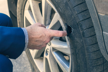 A businessman in a blue suit standing near his car and checks the degree of damage to a punctured...