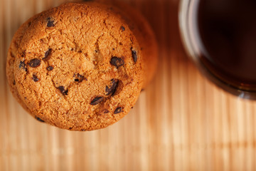 A pile of oatmeal cookies with chocolate chips and a mug of fragrant black hot tea in on a bamboo substrate, on a dark background. Handmade cookies for a healthy breakfast.