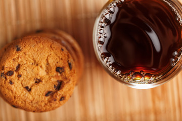 A pile of oatmeal cookies with chocolate chips and a mug of fragrant black hot tea in on a bamboo substrate, on a dark background. Handmade cookies for a healthy breakfast.