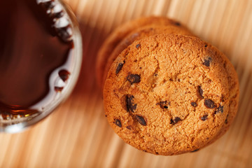 A pile of oatmeal cookies with chocolate chips and a mug of fragrant black hot tea in on a bamboo substrate, on a dark background. Handmade cookies for a healthy breakfast.