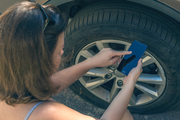 woman crouching near her car with  punctured wheel. girl holding mobile phone and business card with data of isurance company. Concept. mock up - obrazy, fototapety, plakaty
