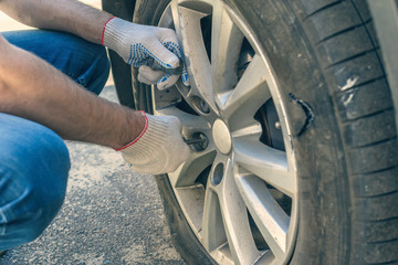 A man in the repair gloves trying to twist off the bolt for changing punctured wheel. Hole in the tire. Concept - obrazy, fototapety, plakaty