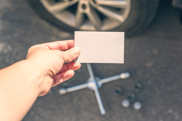 woman crouching near her car with  punctured wheel. girl holding business card with data of isurance company. Concept. mock up - obrazy, fototapety, plakaty