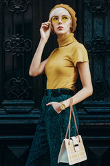 Outdoor fashion portrait of young elegant lady wearing colorful outfit: yellow beret, glasses,...