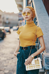 Outdoor fashion portrait of young elegant lady wearing colorful outfit: yellow beret, glasses,...
