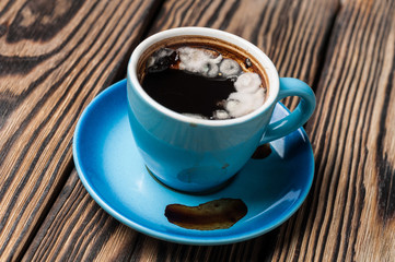 Full dirty blue cup of bad black coffee with mold lies on brown wooden table