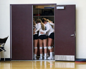A high school volleyball team huddles up in a closet prior to a match.