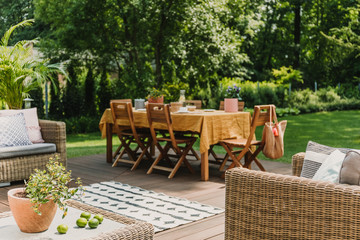 Blurred view of Dining table covered with orange tablecloth standing on wooden terrace in green garden