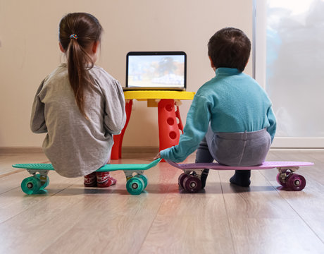 Small children are watching cartoon sitting on the skateboards at home