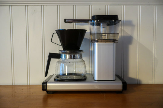A coffee maker i standing on a wooden kitchen counter while the hot water is hitting the powder before the liquid hits the pot.