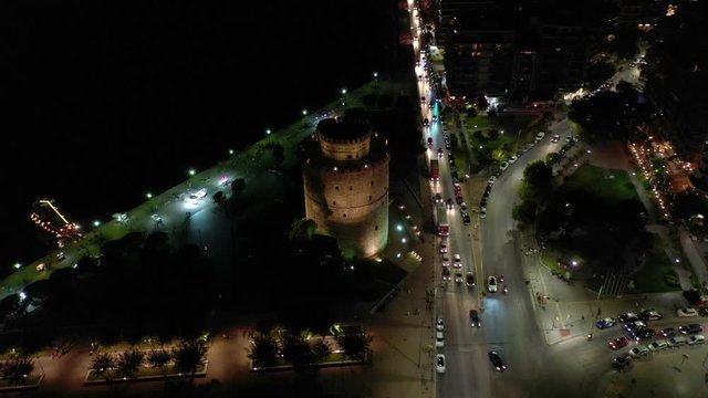 Aerial drone night video of iconic illuminated historic landmark - old byzantine White Tower of Thessaloniki or Salonica, North Greece
