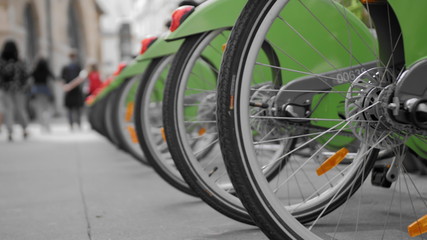 Fototapeta premium Many bikes for rent on the streets of Paris. Close-up rear wheel. Against the background go unrecognized people. The concept of a healthy lifestyle. Slow Motion.
