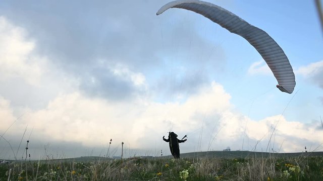 A male athlete paraglider raises a wing in an outdor against the backdrop of evening clouds but cannot fly. Failure while trying to take off