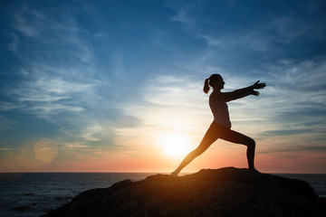 Fototapeta na wymiar Yoga girl silhouette doing fitness exercises on the ocean beach during fantastic sunset.