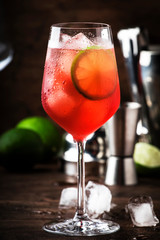 Campari tonic alcoholic cocktail with red bitter, tonic, lime and ice. Old wooden table background, bar tools, selective focus. All names refer to cocktails, not trademarks