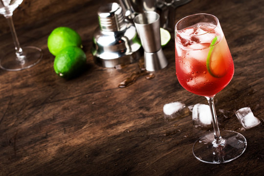 Campari tonic alcoholic cocktail with red bitter, tonic, lime and ice. Old wooden table background, bar tools, selective focus. All names refer to cocktails, not trademarks