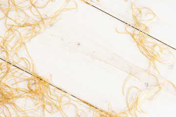 Lot of pieces of thin raw pasta noodles copyspace in middle flatlay on white wood