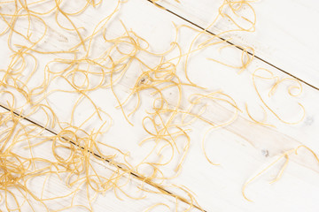 Lot of pieces of thin raw pasta noodles flatlay on white wood