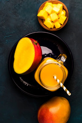 Obraz na płótnie Canvas Mango smoothie in glass jar with fresh fruit on blue background, copy space, top view